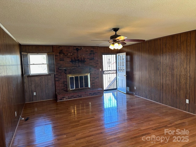 unfurnished living room featuring dark wood-type flooring, a textured ceiling, a brick fireplace, and wood walls