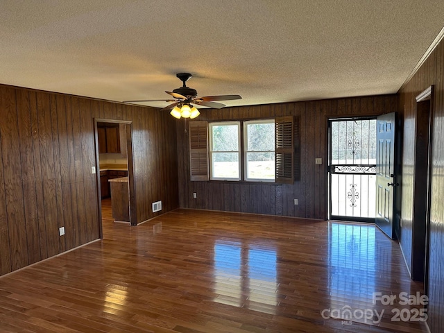 unfurnished room with dark wood-type flooring, wooden walls, a textured ceiling, and ceiling fan