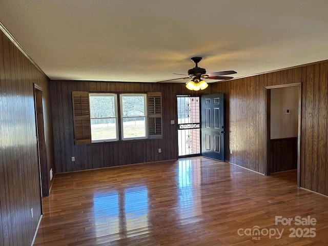 unfurnished room featuring dark wood-type flooring, ceiling fan, wooden walls, and a textured ceiling