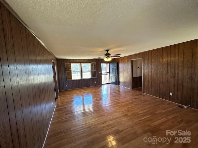 spare room with hardwood / wood-style flooring, ceiling fan, wooden walls, and a textured ceiling