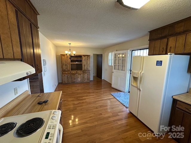 kitchen with hanging light fixtures, hardwood / wood-style flooring, exhaust hood, white appliances, and an inviting chandelier