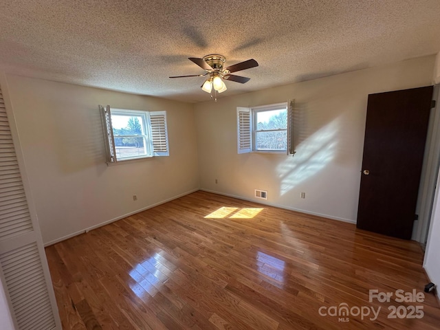 unfurnished bedroom with multiple windows, ceiling fan, hardwood / wood-style flooring, and a textured ceiling