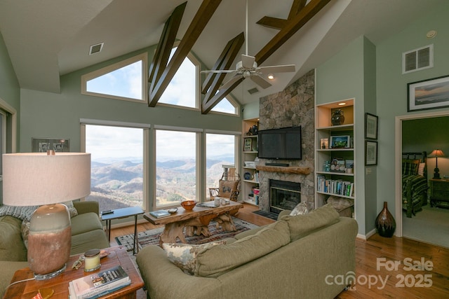 living room featuring a stone fireplace, hardwood / wood-style floors, high vaulted ceiling, ceiling fan, and beam ceiling