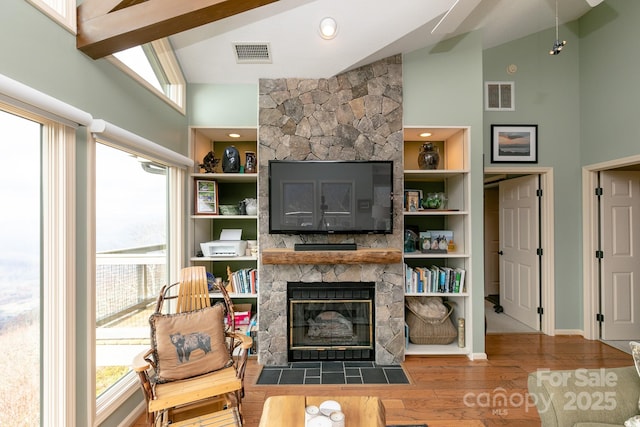 living room featuring wood-type flooring, a stone fireplace, built in features, and high vaulted ceiling