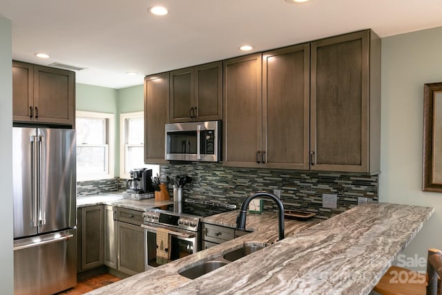 kitchen featuring appliances with stainless steel finishes, light stone countertops, sink, and decorative backsplash