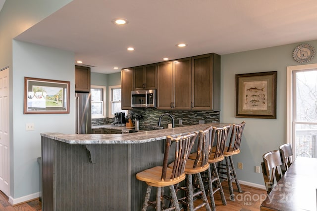 kitchen featuring a breakfast bar area, light hardwood / wood-style flooring, kitchen peninsula, stainless steel appliances, and decorative backsplash