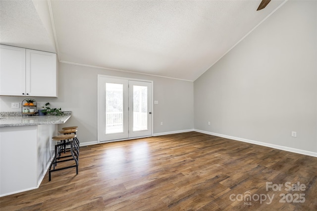 unfurnished living room with a textured ceiling, wood finished floors, baseboards, vaulted ceiling, and crown molding