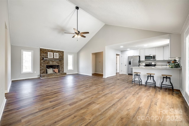 unfurnished living room featuring a brick fireplace, ceiling fan, baseboards, and wood finished floors