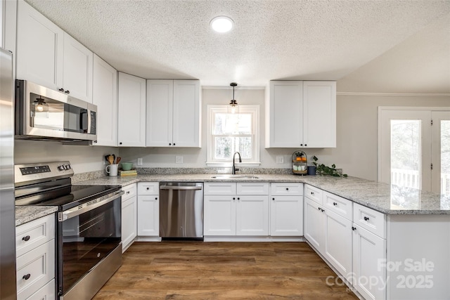 kitchen with appliances with stainless steel finishes, dark wood-type flooring, a peninsula, white cabinetry, and a sink