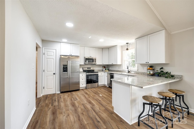 kitchen featuring white cabinets, appliances with stainless steel finishes, a peninsula, a kitchen bar, and a sink