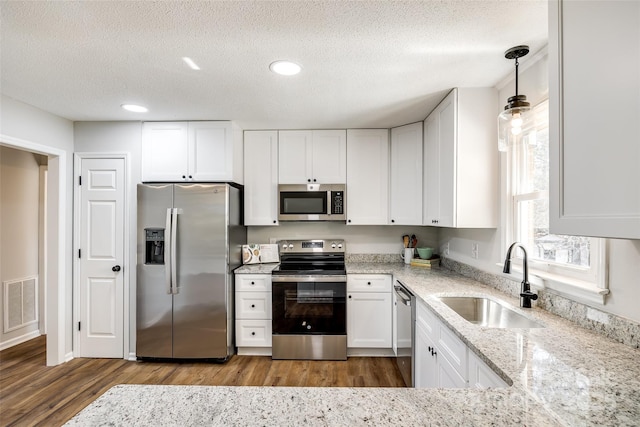 kitchen featuring stainless steel appliances, wood finished floors, a sink, visible vents, and white cabinetry