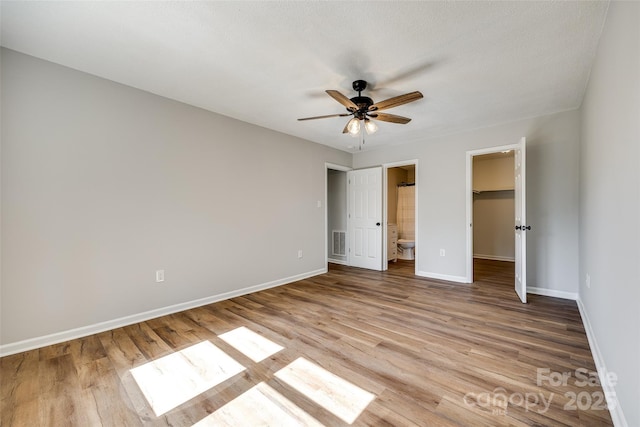 unfurnished bedroom featuring visible vents, a spacious closet, ensuite bathroom, light wood-type flooring, and baseboards