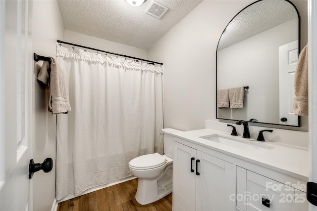 bathroom with a textured ceiling, toilet, wood finished floors, vanity, and visible vents