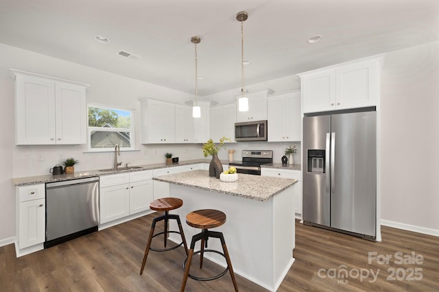 kitchen with sink, decorative light fixtures, appliances with stainless steel finishes, a kitchen island, and white cabinets