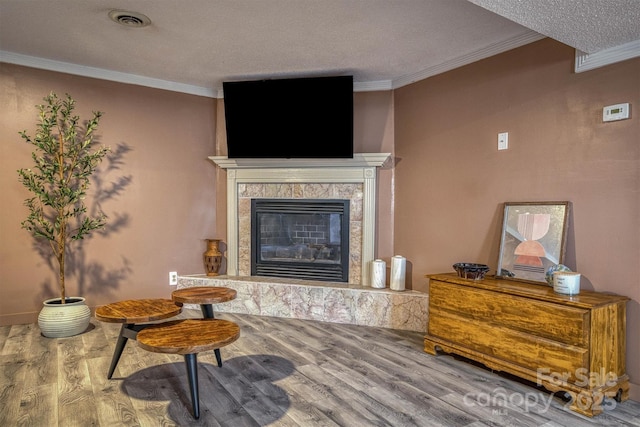 sitting room featuring a tiled fireplace, crown molding, hardwood / wood-style flooring, and a textured ceiling