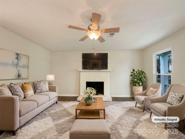 living room with ceiling fan, a fireplace, hardwood / wood-style floors, and a textured ceiling