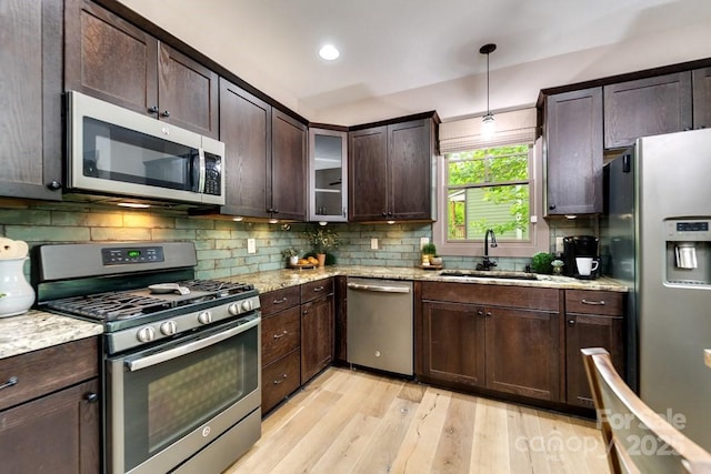 kitchen featuring sink, hanging light fixtures, dark brown cabinets, stainless steel appliances, and light stone countertops