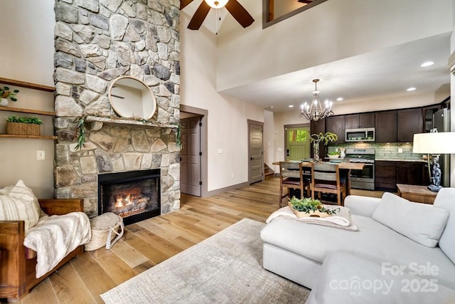 living room featuring a stone fireplace, light hardwood / wood-style flooring, and ceiling fan with notable chandelier