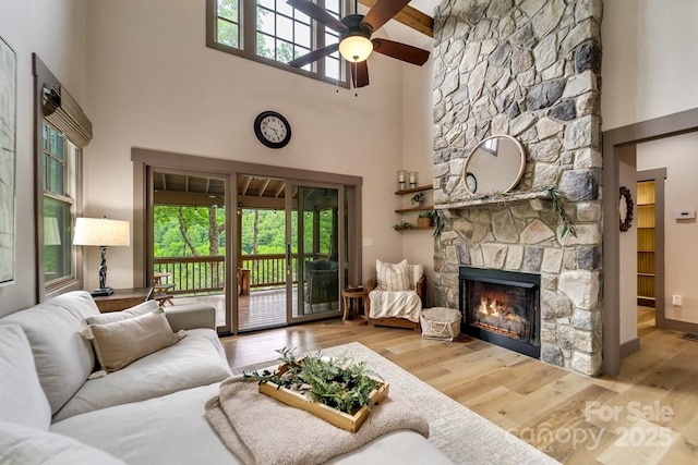 living room featuring a high ceiling, a stone fireplace, ceiling fan, and hardwood / wood-style flooring