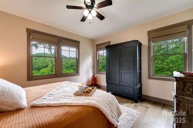 bedroom featuring ceiling fan, light hardwood / wood-style floors, and multiple windows