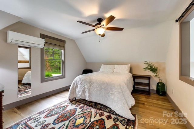 bedroom featuring lofted ceiling, a wall mounted air conditioner, light wood-type flooring, ceiling fan, and a barn door