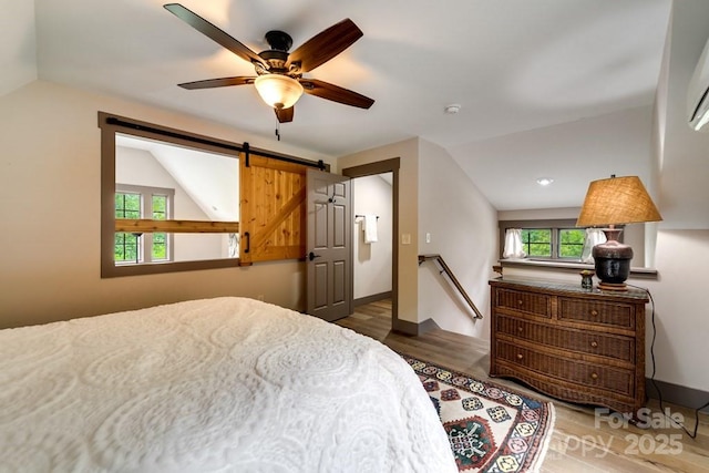 bedroom with a barn door, lofted ceiling, dark wood-type flooring, and ceiling fan