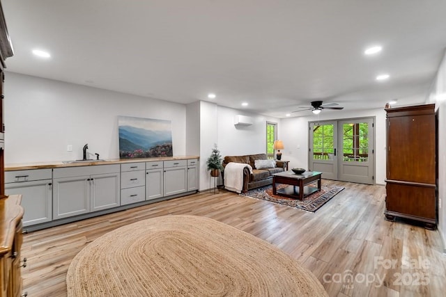 living room with sink, light hardwood / wood-style flooring, ceiling fan, a wall unit AC, and french doors