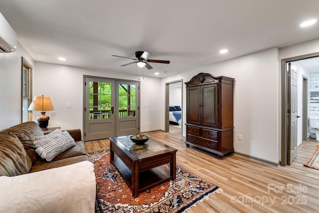 living room with a wall mounted air conditioner, light hardwood / wood-style floors, french doors, and ceiling fan