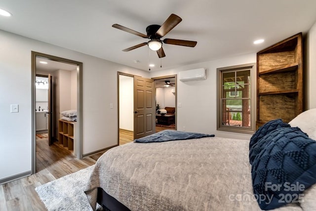 bedroom featuring ceiling fan, a wall mounted AC, light hardwood / wood-style floors, and ensuite bath