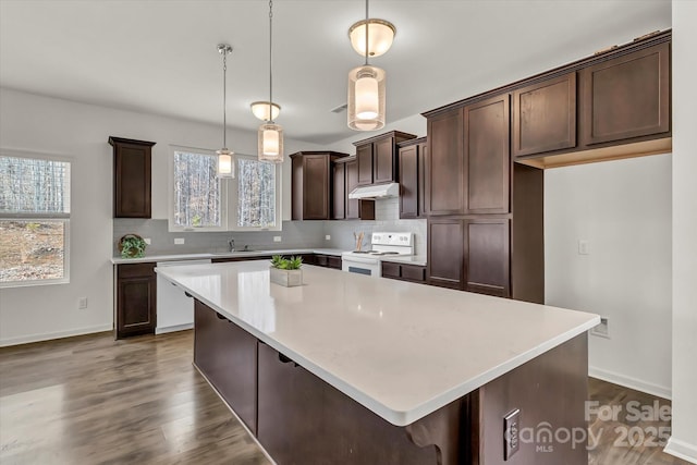 kitchen featuring dark brown cabinets, white appliances, pendant lighting, a center island, and a healthy amount of sunlight