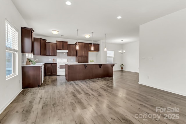 kitchen featuring backsplash, white range with electric stovetop, a kitchen island, decorative light fixtures, and light hardwood / wood-style floors