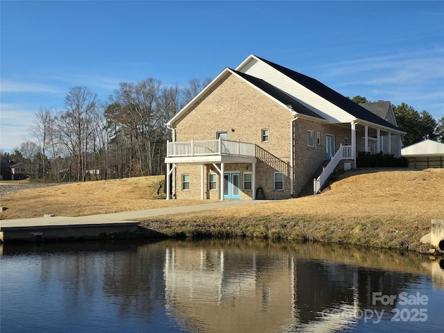 rear view of house with brick siding and a deck with water view