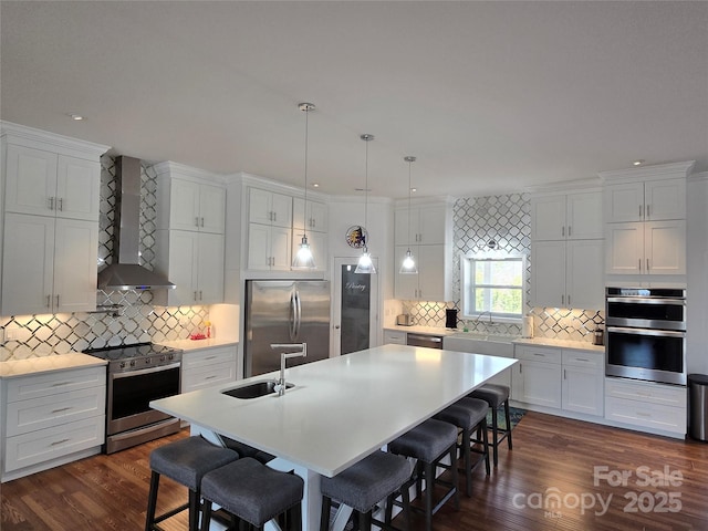 kitchen featuring a breakfast bar area, stainless steel appliances, a sink, wall chimney exhaust hood, and a center island with sink