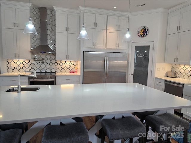 kitchen featuring stainless steel appliances, light countertops, visible vents, wall chimney range hood, and a kitchen breakfast bar