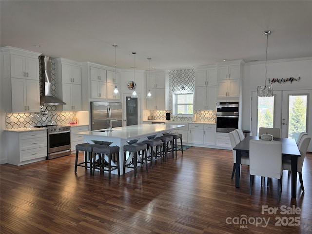 kitchen with stainless steel appliances, wall chimney range hood, a breakfast bar, and white cabinetry