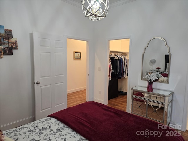 bedroom featuring baseboards, ornamental molding, a notable chandelier, a walk in closet, and a closet