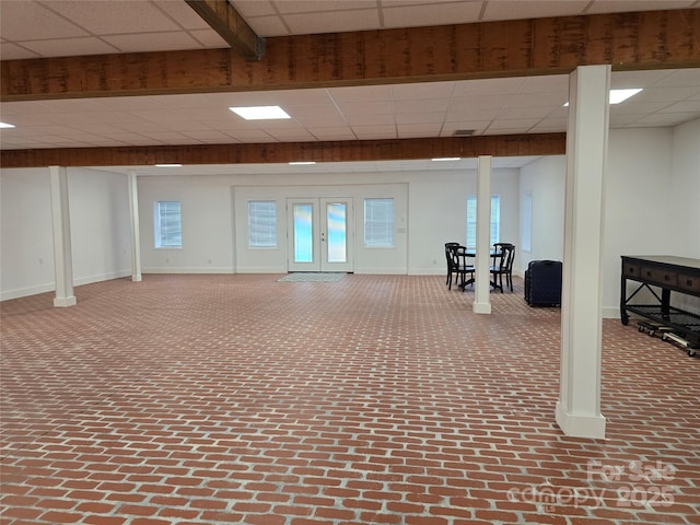 below grade area featuring brick floor, baseboards, a drop ceiling, and french doors