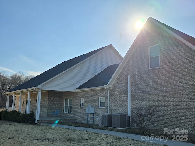 back of house featuring covered porch, central AC unit, and brick siding