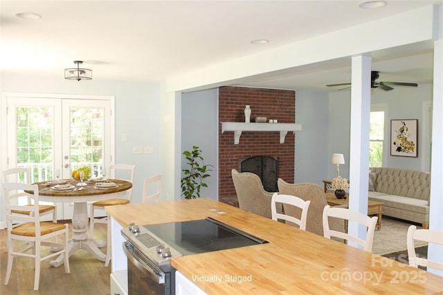 kitchen with stainless steel electric range, wood-type flooring, ceiling fan, a brick fireplace, and french doors