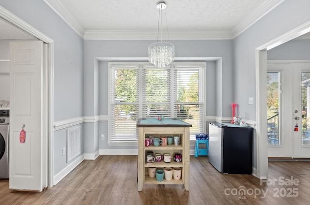 dining area featuring washer / clothes dryer, ornamental molding, a chandelier, and light hardwood / wood-style flooring