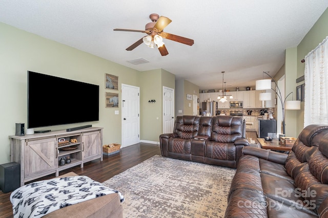 living room with ceiling fan with notable chandelier, dark wood-type flooring, and a textured ceiling