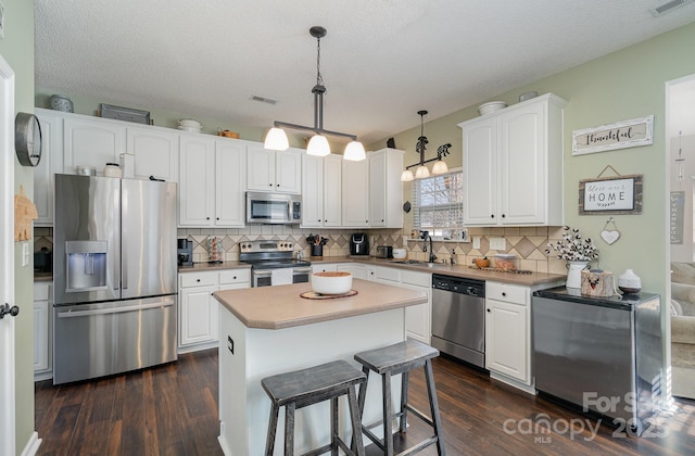 kitchen featuring stainless steel appliances, a kitchen island, hanging light fixtures, and white cabinets