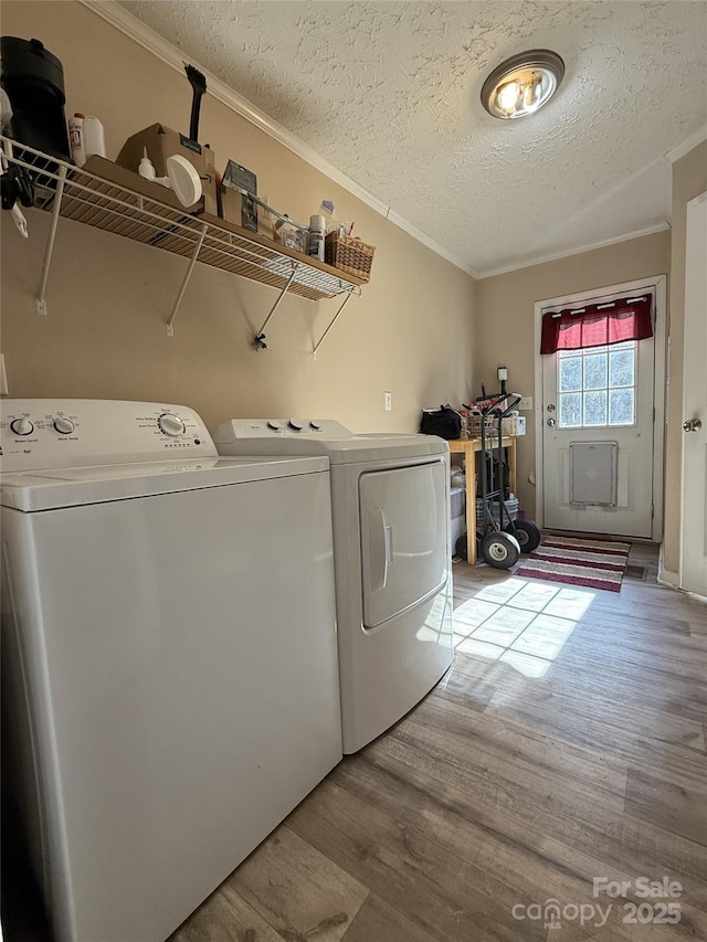 clothes washing area featuring crown molding, washing machine and dryer, a textured ceiling, and light wood-type flooring