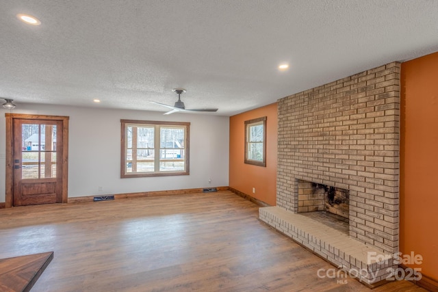 unfurnished living room with a wealth of natural light, a fireplace, light hardwood / wood-style floors, and a textured ceiling