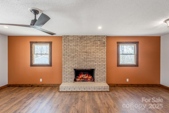 unfurnished living room featuring wood-type flooring, ceiling fan, a textured ceiling, and a fireplace