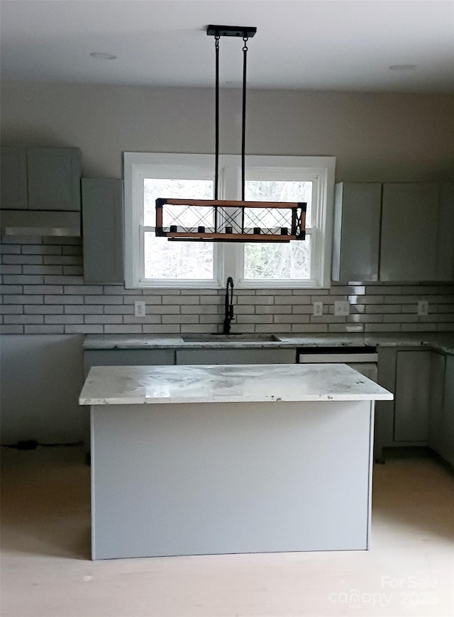 kitchen featuring light stone counters, backsplash, a sink, and a center island