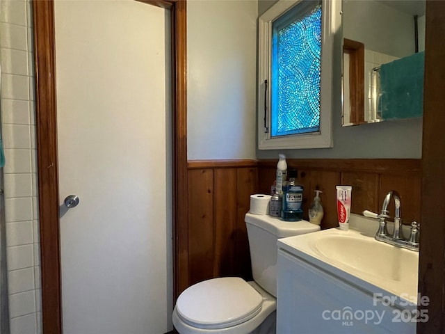 bathroom with toilet, vanity, and wood walls