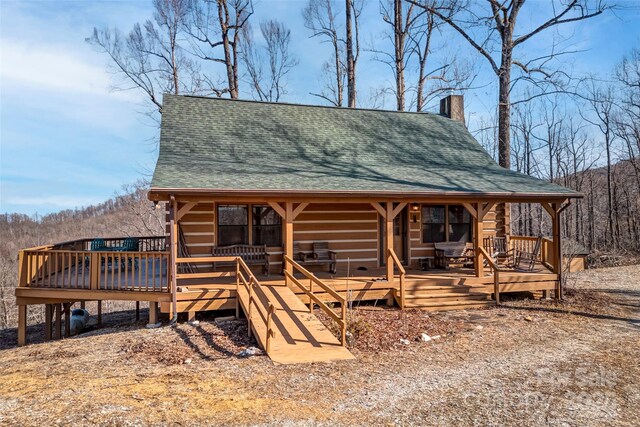 log home featuring log exterior, a shingled roof, a chimney, and a wooden deck