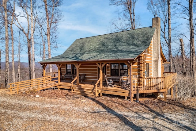 log-style house featuring a shingled roof, a chimney, a deck, and log exterior