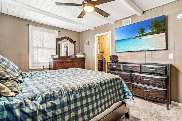 bedroom with ceiling fan, beam ceiling, light carpet, and wood walls